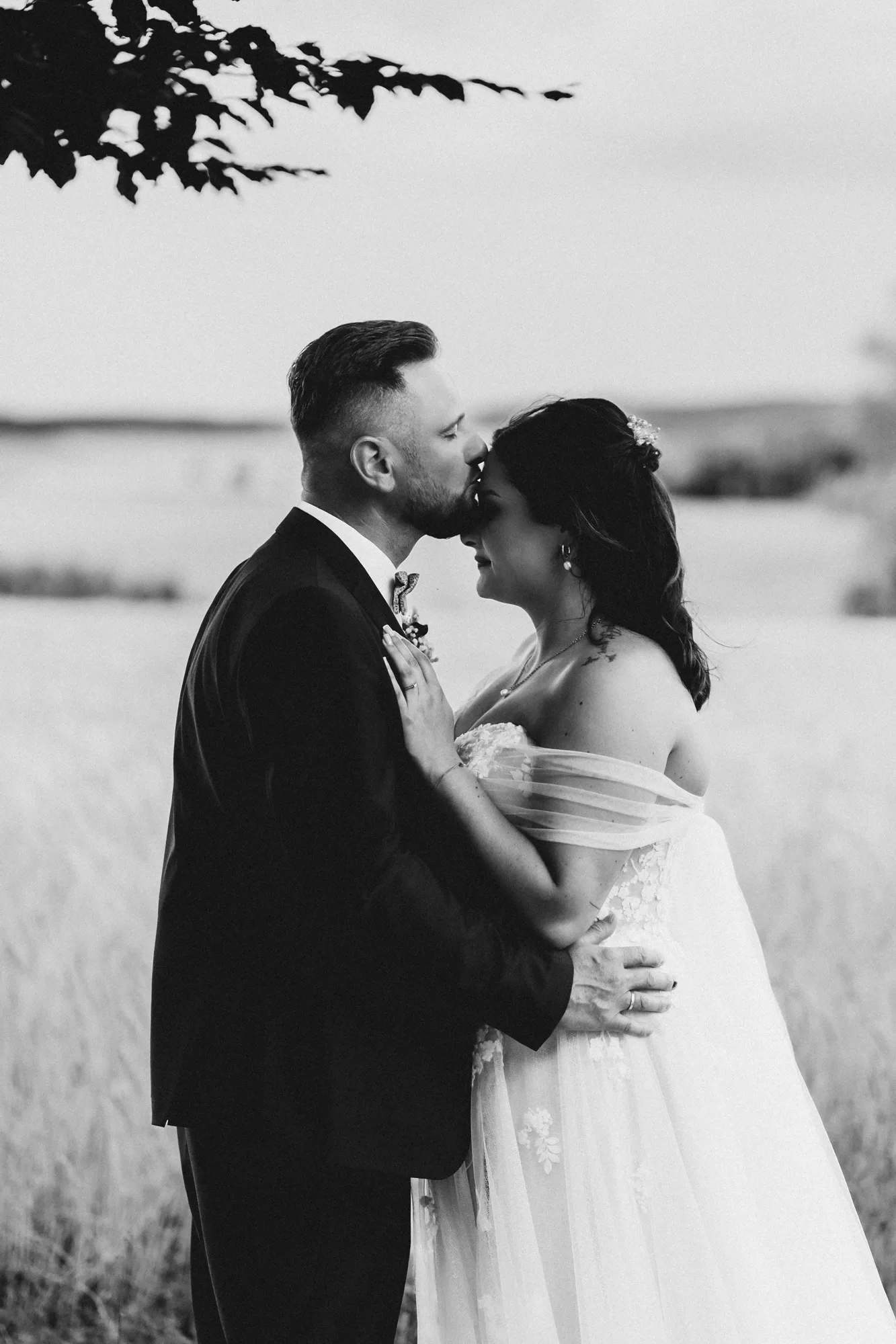 Schwarz-weiß-Aufnahme: Brautpaar Stirn an Stirn im Feld — Hochzeitsfotografie Jacqueline & Sascha in Berg