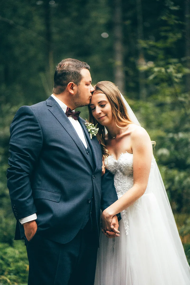Bräutigam küsst die Braut zärtlich auf die Stirn im Wald — Hochzeitsfotograf Oberfranken